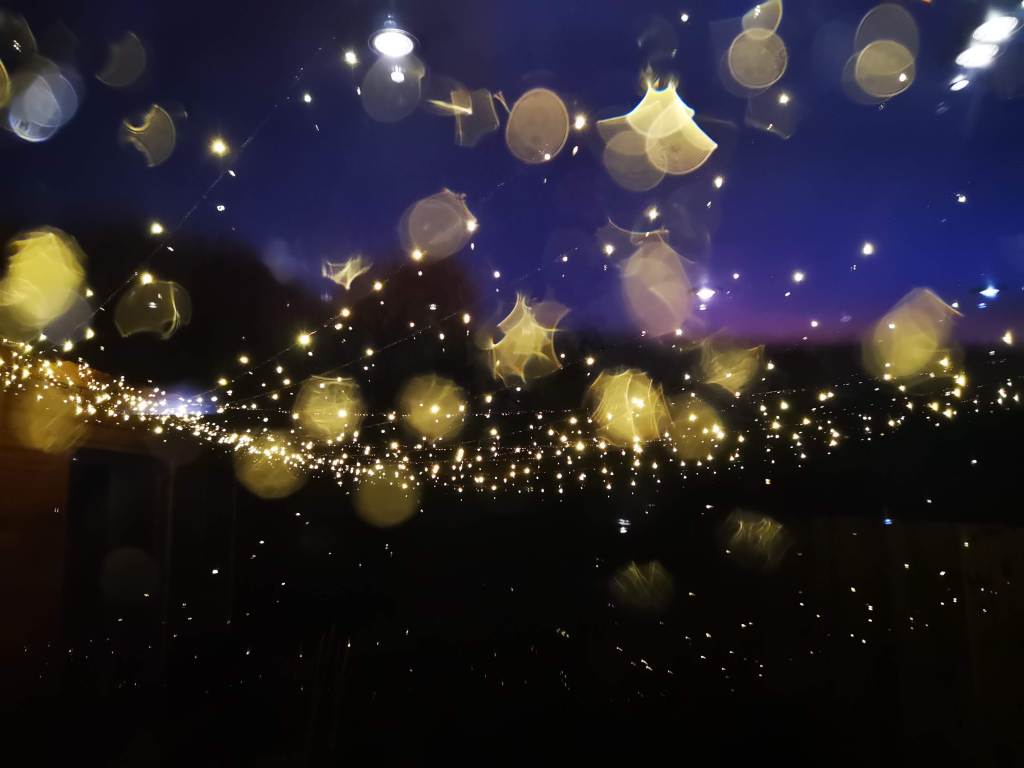 A photo taken during a rainy night, I held the lens right at the glass pane from the insight, outside the fairy lights are caught in the rain drops on the glass and create interesting fractions of light on the window pane. It's like looking through a kaleidoscope